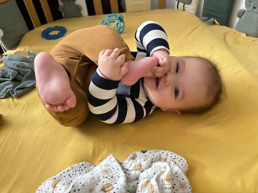 Kind liegt auf dem Rücken und spielt mit Händen und Füßen.